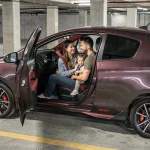 Famille urbaine installée dans une Toyota Yaris Sport rouge et noire dans un parking souterrain