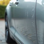 Stylo efface-rayures posé sur une portière de voiture argentée rayée avec un chiffon microfibre