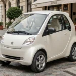 Voiture sans permis 4 places neuve garée en ville, modèle compact blanc nacré vue de trois quarts