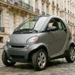Voiture sans permis manuelle grise garée dans une rue pavée française avec bâtiments en pierre en arrière-plan